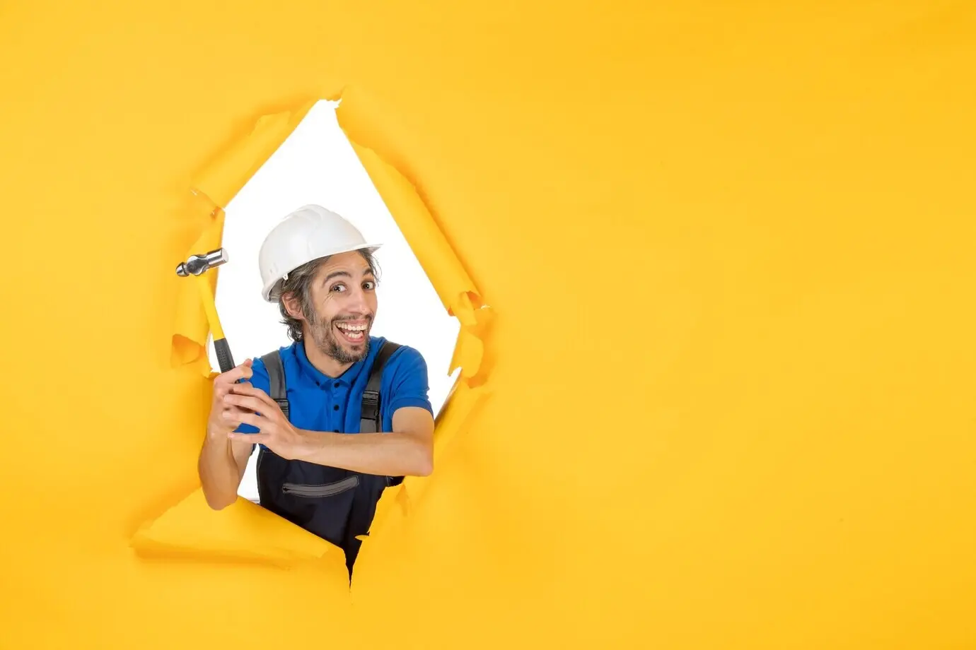 Vorderansicht eines männlichen Bauarbeiters in Uniform mit Hammer vor gelber Wand.